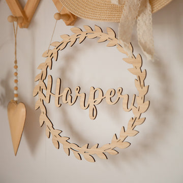 A Personalised Flora Name Wreath with "Harper" in cursive hangs on the wall amid neutral nursery decor like a straw hat and wooden heart—perfect bamboo wall art to create a cozy space.