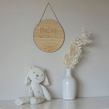 A soft white stuffed bunny sits beside a white vase with dried pale foliage on a white surface. Above them, a round Personalised Sunflower Plaque hangs on the wall.