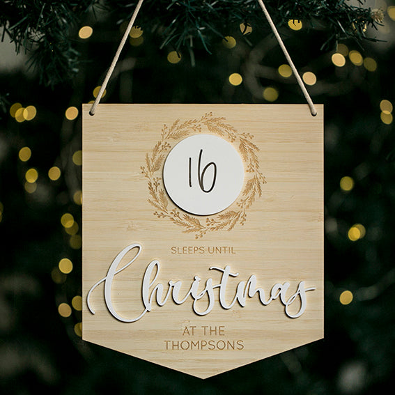 The Christmas Countdown Banner hangs on a tree with fairy lights, displaying "16 sleeps until Christmas at the Thompsons"—16 in a white circle and Christmas in large cursive—a unique personalised festive decoration.