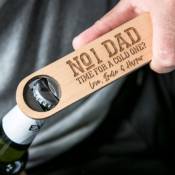 A hand uses the Personalised Bottle Opener (3 designs available), engraved with "No1 Dad, Time for a cold one? Love, Indie & Harper," to open a green beer bottle—a practical gift for men who value thoughtful details.