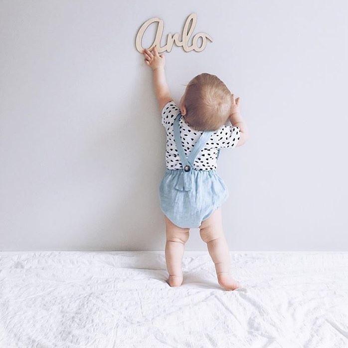 A wooden wall name saying Arlo, with a baby reaching up to it. 