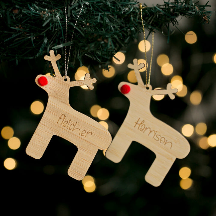 Two wooden reindeer Christmas ornaments with personalized engravings, hanging from a tree with holiday lights.