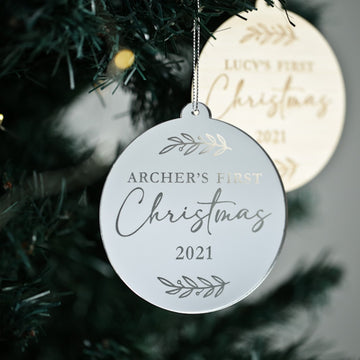 A close-up of the First Christmas Laurel Christmas Bauble reads Archer’s First Christmas 2021, with a gold ornament in the background—a perfect keepsake gift for celebrating baby’s first holiday season.