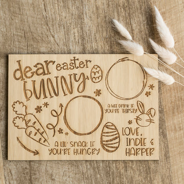 The Personalised Easter Bunny Treat Board is a wooden board with engraved spaces for a drink, snack, and egg, cute carrot and egg doodles, "Dear Easter Bunny," "Love, Indie & Harper," and pampas grass in the corner.