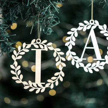 The Alpha Wreath Christmas Bauble, featuring cut-out initials I and A, hangs on a tree—personalised ornaments glowing softly against blurred golden lights.