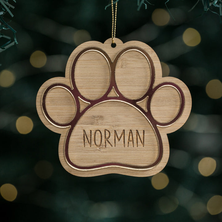 A personalized wooden Christmas ornament in the shape of a paw print with the name &