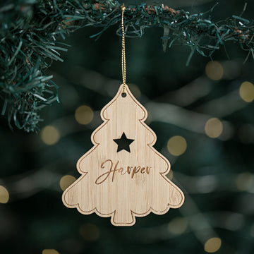 A personalized Christmas tree ornament with a wooden tree shape, star cut out, and the name &