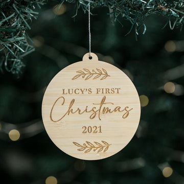 A round Christmas bauble with a bamboo-like texture, hanging from a tree. It has the text &