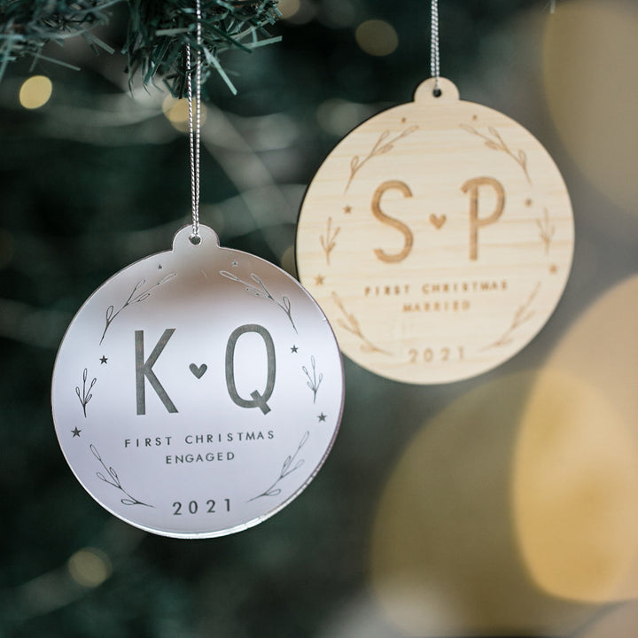Two Lovers Christmas Baubles hang on a tree—one reads "K♥Q First Christmas Engaged 2021," the other "S♥P First Christmas Married 2021." With simple leafy designs, they&