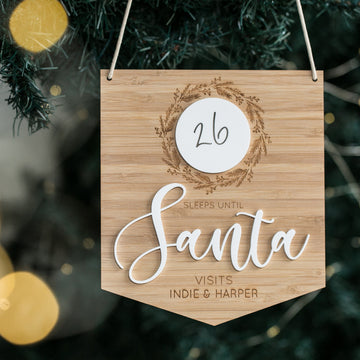 The Christmas Countdown Banner is a personalised bamboo tree decoration that features “26 sleeps until Santa visits Indie & Harper” in large script with a festive wreath, making it the perfect countdown plaque for the holidays.
