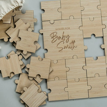 The Personalised Guestbook Jigsaw Puzzle features several loose wooden pieces, with a center piece engraved "Wishes for Baby Smith" in script. A fabric bag is partially visible in the top left corner.