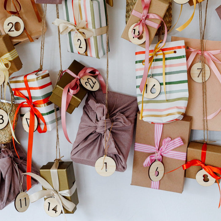 The Advent Calendar Tags Set, with wrapped gifts in assorted patterns each adorned with round wooden tags, hanging against a white background.