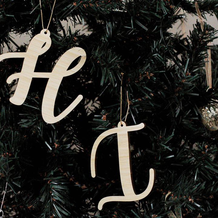Two Letter Christmas Ornaments hang on a dark green Christmas tree. Each ornament is attached with gold string and surrounded by festive branches, adding a personalized touch to your holiday décor.