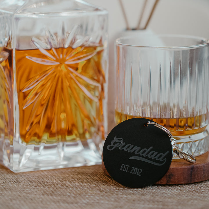 Black Grandad est. 2012 keyring, in front of a whiskey decanter and glass. 