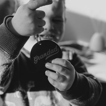 Black and white photo of boy holding a black keyring saying Grandad.