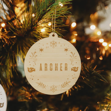 A round Christmas bauble with a winter wonderland styled wreath and the word &