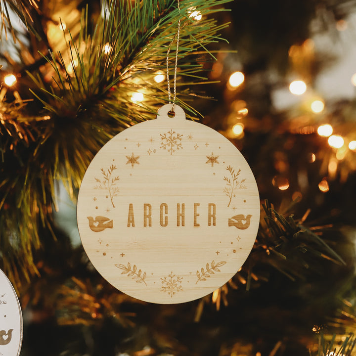 A round Christmas bauble with a winter wonderland styled wreath and the word &