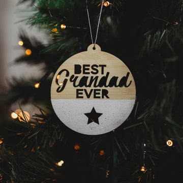 A round Christmas ornament with a bamboo exterior, white glitter and text that reads &