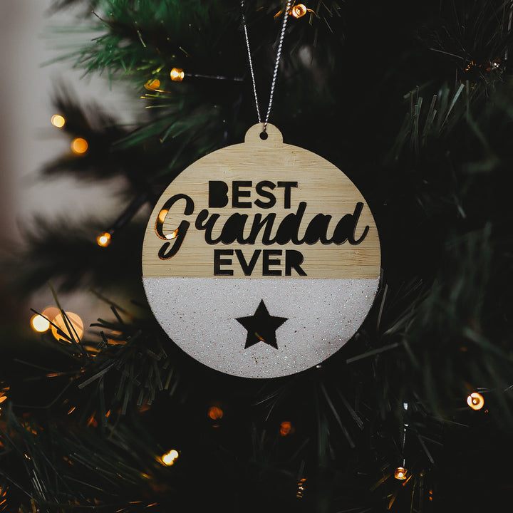 A round Christmas ornament with a bamboo exterior, white glitter and text that reads &