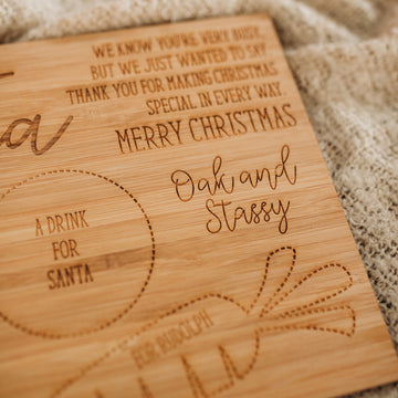 The Personalised Santa Treat Board features engraved spaces for "A drink for Santa" and "For Rudolph," plus a Merry Christmas message and Oak and Stassy branding—perfect for creating a cherished Christmas tradition. Placed on textured beige fabric.