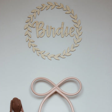 A leafy-look bamboo wreath, surrounding a bamboo personalised wall name saying Birdie. Hanging in a child&