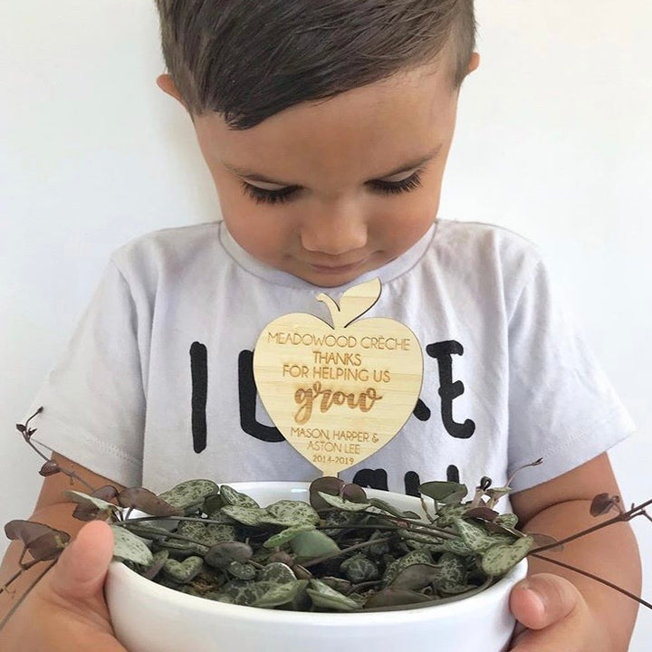 A young boy looks down at a white bowl with a leafy plant, holding a Personalised Teacher Planter engraved with “MEADOWOOD CRECHE THANKS FOR HELPING US GROW MASON HARDER & JASON LEE 2018-2019.”.