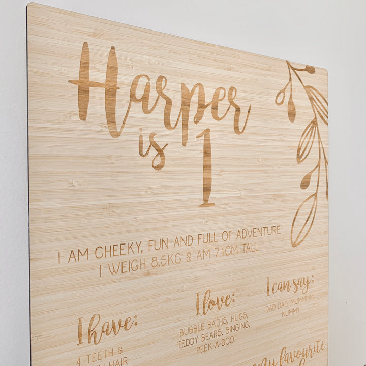 A large bamboo sign engraved with a vine and Harper is 1. Also engraved with I love, I can say, I love to eat, I am good at and my favourite book.