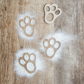 An MDF Easter bunny stencil, lying on the ground next to three bunny foot prints made with flour.