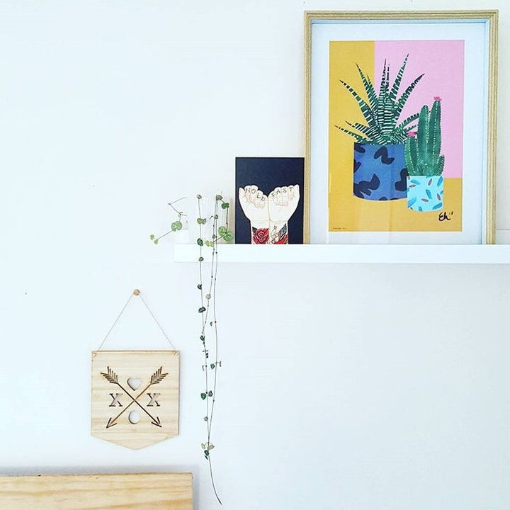 A white floating shelf displays a framed plant print, foot art, and a potted trailing plant. Beneath, the XOX Crest Banner with geometric designs.
