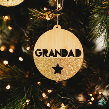 The Glittered Christmas Bauble is a round bamboo ornament with GRANDAD in bold and a black star, half covered in gold glitter—perfect for adding a personalised festive touch to your decorated holiday tree.