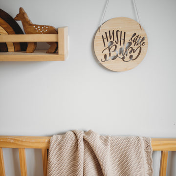 A round light bamboo sign saying hush little baby. Hanging in a child&