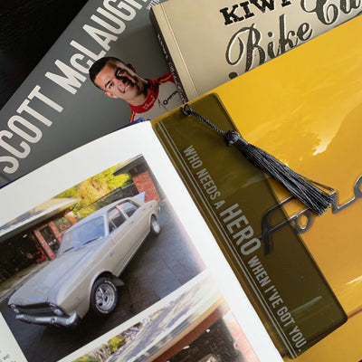 A black see through acrylic bookmark with black tassel, saying who needs a hero when I've got you. Sitting on a cars book.