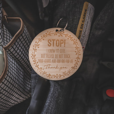 A round dark bamboo keyring with a floral wreath, saying Stop! I know I'm cute, but please do not touch. Your germs are too big for me. Thank you. Attached to a baby capsule. 