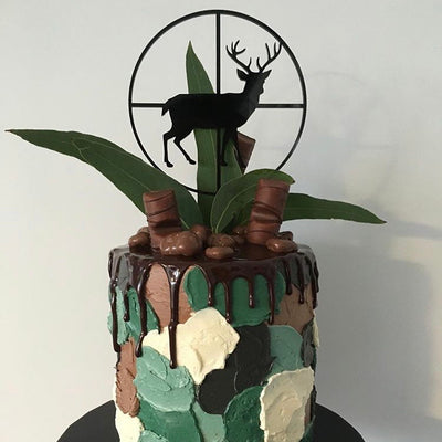 A black acrylic stag shaped cake topper as if looking through a gun cross section. Sitting on a green camo style cake.