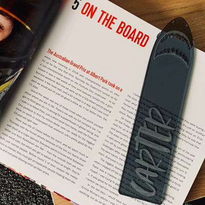 A black see through acrylic bookmark in the shape of a sharks jaw, with the name Carter etched on there. 