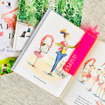 A neon pink see through acrylic bookmark with a unicorns head at the end, and the name Harper etched on, sitting atop a children&