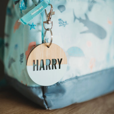 A round light bamboo keyring, half painted blue, saying Harry. Attached to a blue under the sea school bag. 