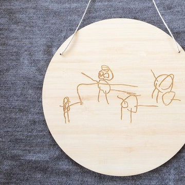 A round light bamboo plaque with a childs drawing engraved on it. 