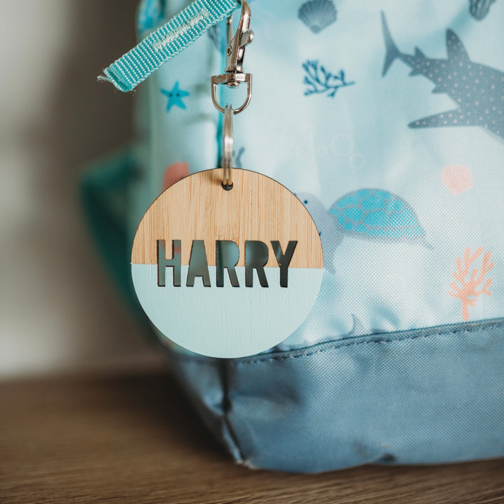 A round light bamboo keyring, half painted blue, saying Harry. Attached to a blue under the sea school bag.