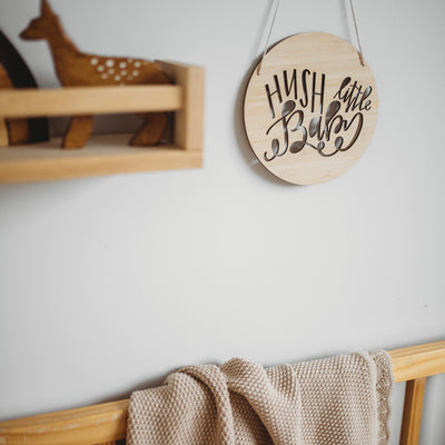 A round light bamboo sign saying hush little baby. Hanging in a child's nursery. 