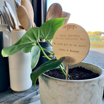 The Personalised Gift Planter, featuring a wooden "Happy Birthday to our beautiful Nan" sign from Indie & Harper, sits on a windowsill by kitchen utensils—a heartfelt present for your loved one.