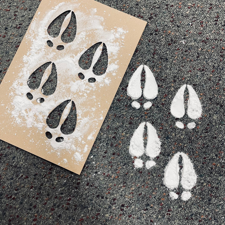 The Reindeer Hoofprints Stencil rests on a speckled carpet, with four white powdered hoof prints made using the stencil—a festive touch perfect for Christmas yard decorations.