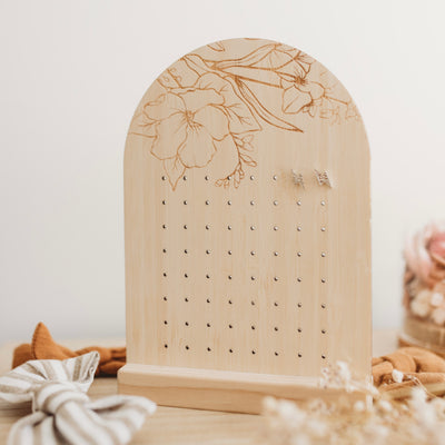 An arch shaped bamboo earring holder with a floral design etched on the top. Surrounded by hairbows.