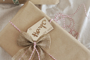 A gift wrapped in brown paper with red and white twine, finished with a burlap bow and our Personalised Gift Tags reading “To Harper, Love, Santa.”.