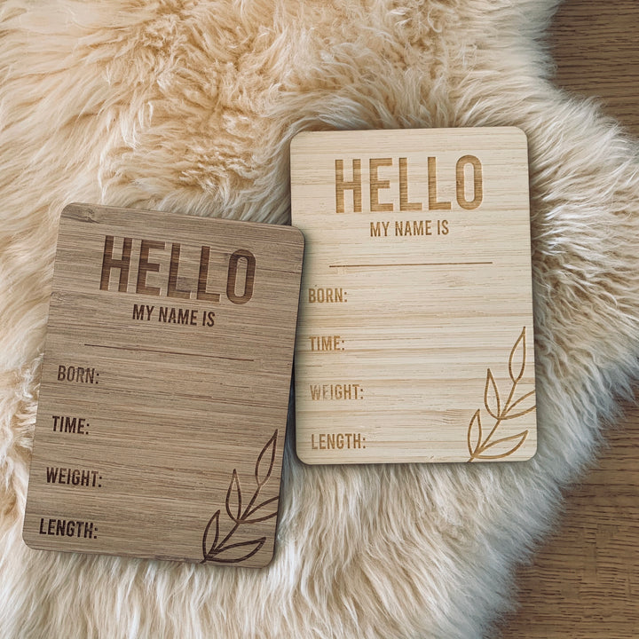 A light bamboo and dark bamboo rectangle birth announcement card saying Hello my name is. Born, Time, Weight and Length. Laying next to each other on a sheepskin rug..
