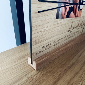 A close-up of the Christmas Photo Holder, made in New Zealand, on a stand with black strings holding a photo and engraved: WE LOVE YOU SO SO SO SO0000 MUCH DADDY. YOU ARE OUR NUMBER 1! LOVE FROM MUM & THE KIDS.
