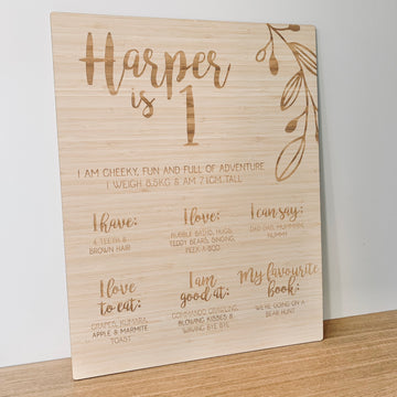A large bamboo sign engraved with a vine and Harper is 1. Also engraved with I love, I can say, I love to eat, I am good at and my favourite book.