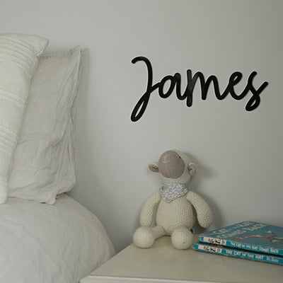 A black acrylic wall name saying James, on the wall of a child's room.