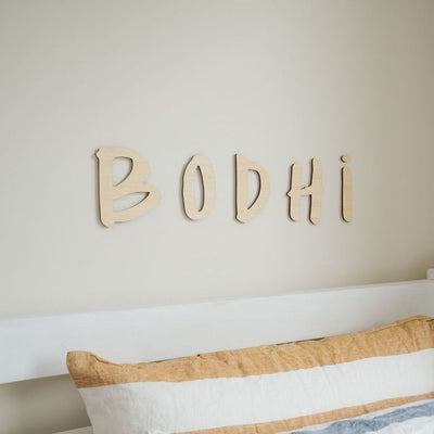 A bamboo hand lettered wall name saying Bodhi, hanging above a bed.