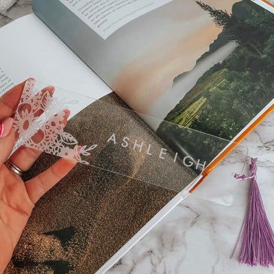 A clear floral bookmark with purple tasel, saying Ashleigh. 